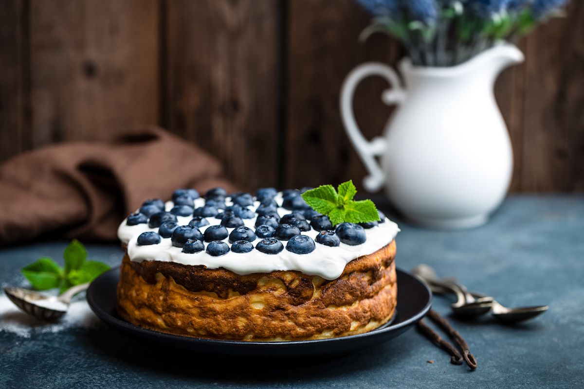 Ein Kuchen mit Blaubeeren und Sahne auf einem schwarzen Teller.