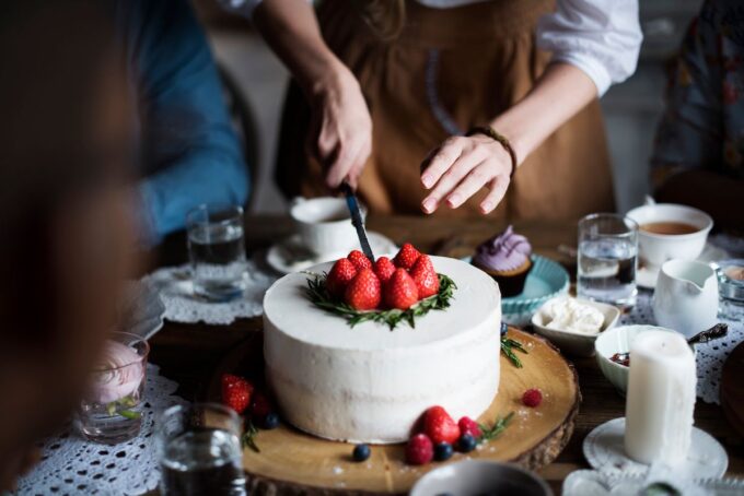 Eine Frau schneidet einen Kuchen mit Erdbeeren darauf an.