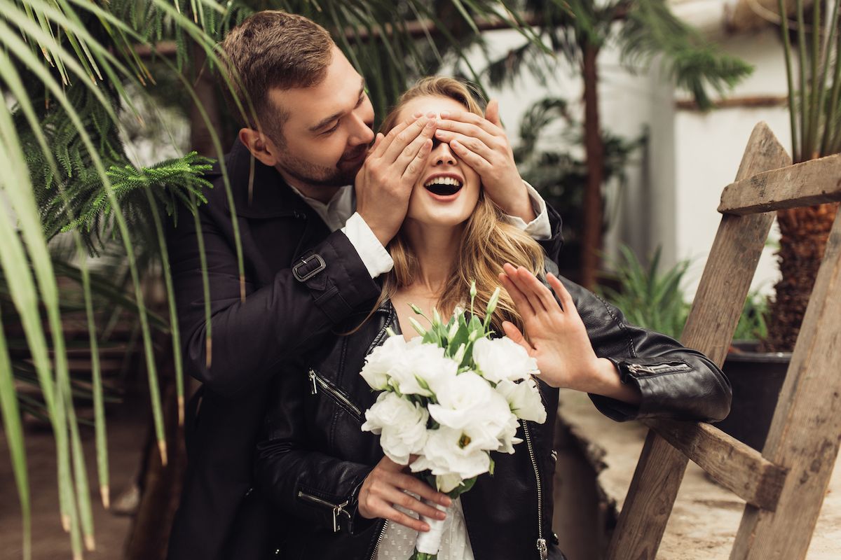 Ein Mann und eine Frau bedecken ihre Gesichter und halten einen Blumenstrauß in der Hand.
