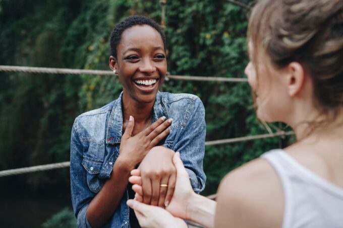 Zwei schwarze Frauen lächeln einander auf einer Brücke an.