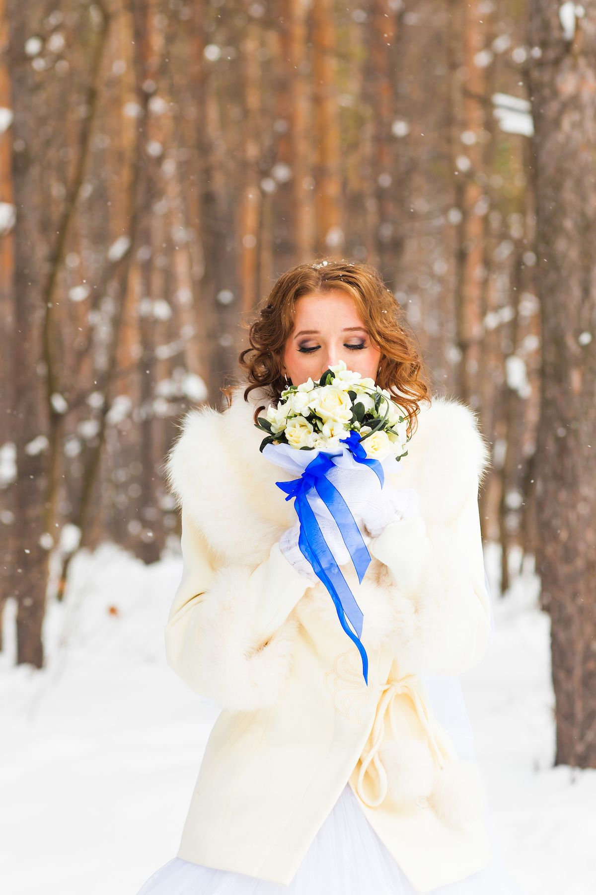Eine Braut hält einen Blumenstrauß im Schnee.