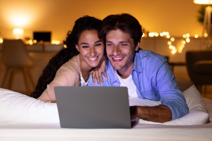 Ein Mann und eine Frau liegen auf einem Bett und benutzen einen Laptop.
