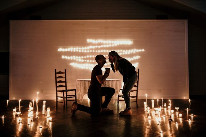 Ein Paar kniet vor einem mit Kerzen erleuchteten Raum nieder.