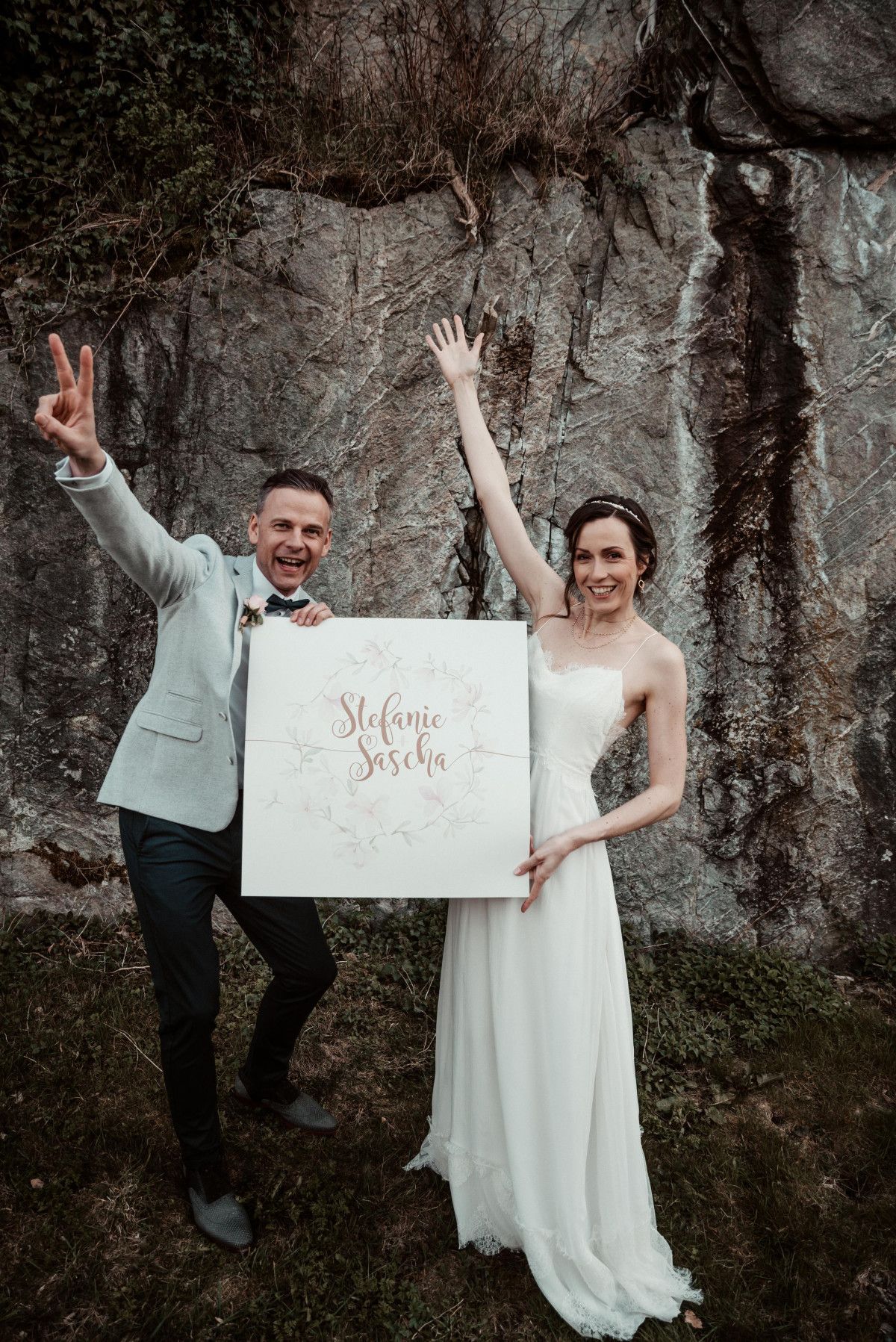 Hochzeitszeitung Ideen: Brautpaar auf ihrer Hochzeit mit einem Bild ihrer Namen in den Händen