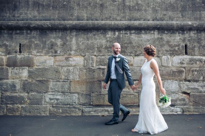 Eine Braut und ein Bräutigam gehen vor einer Steinmauer.