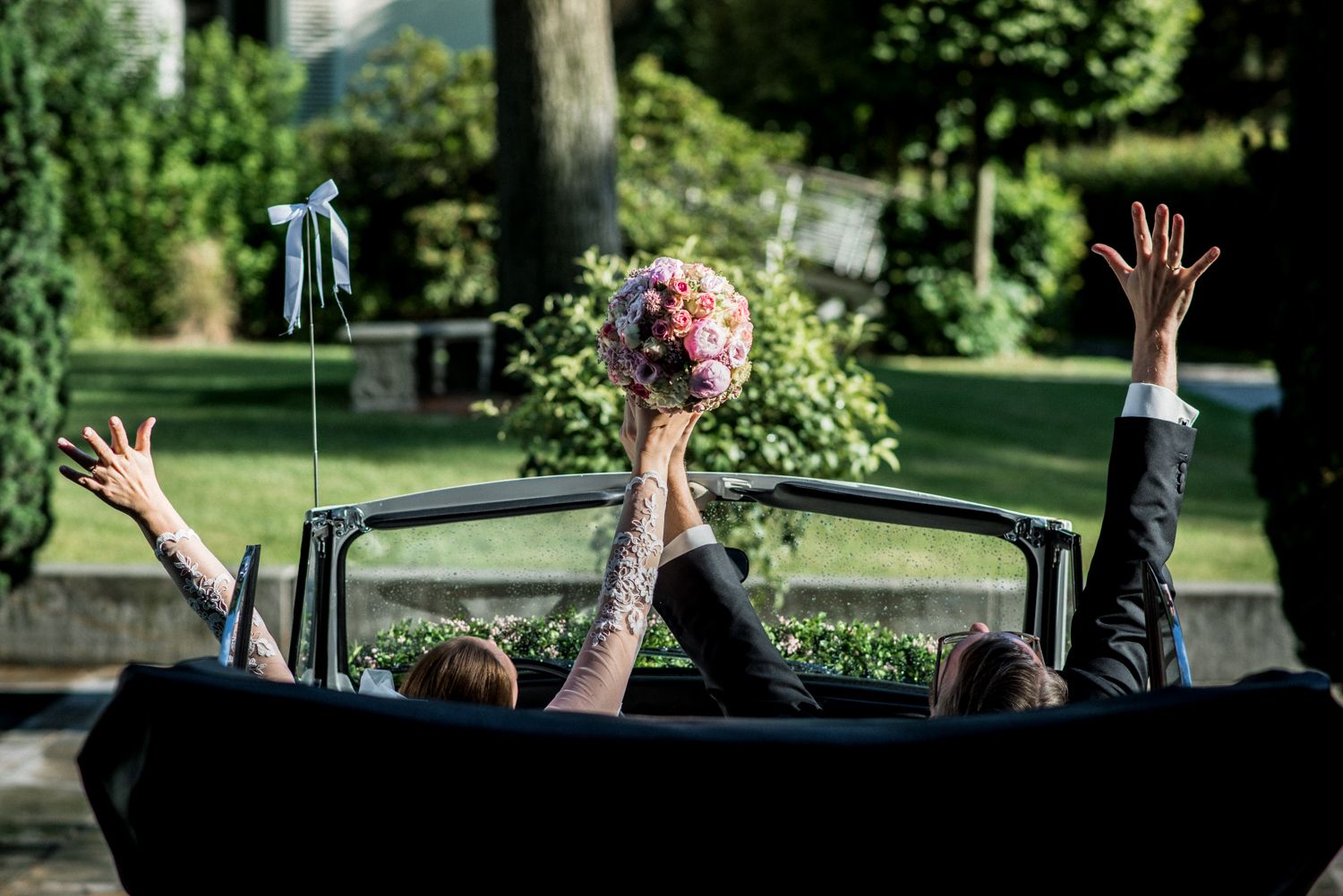 Das Brautpaar sitzt in einem Auto und hält gemeinsam den Brautstrauß.