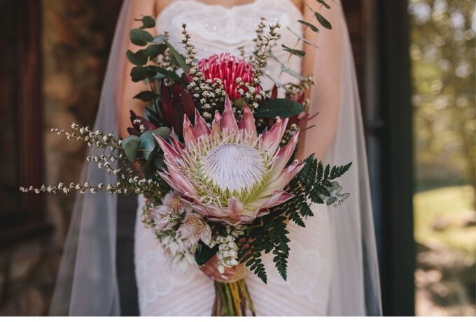 Eine Braut hält einen Strauß Proteas und Eukalyptus.