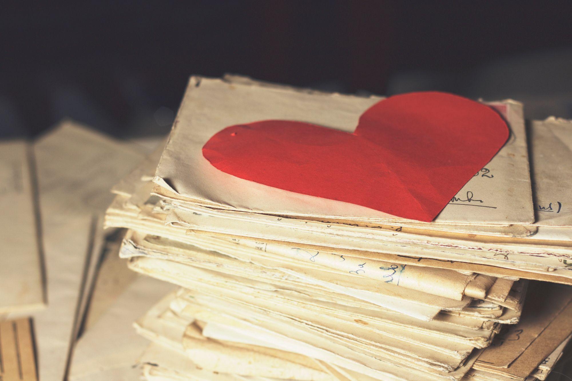 Ein Stapel alter Briefe mit einem roten Herzen obendrauf.