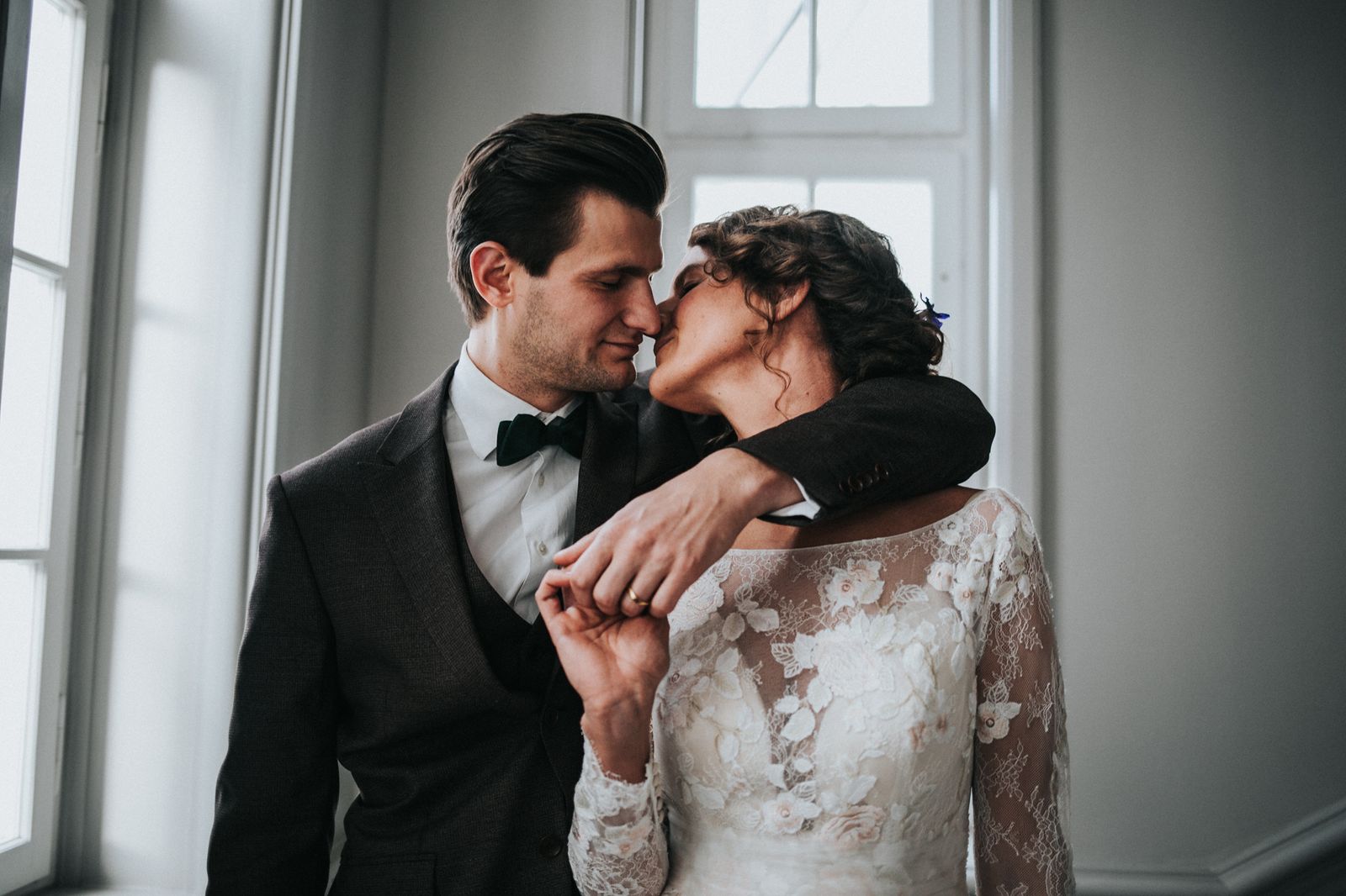 Eine Braut und ein Bräutigam küssen sich vor einem Fenster.