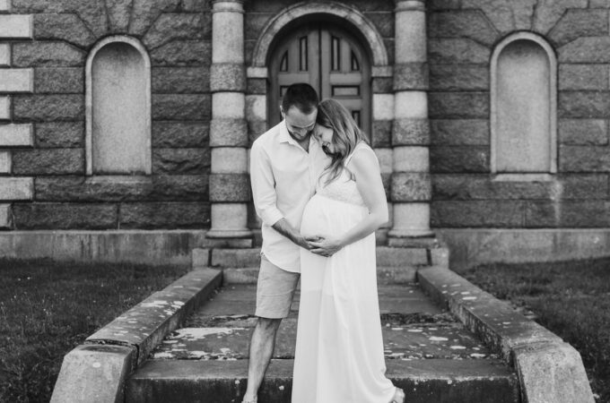 Ein schwangeres Paar steht auf den Stufen eines alten Gebäudes.