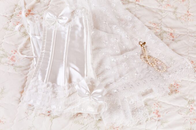 Ein weißes Korsett mit Spitze und Perlen auf einem Bett.