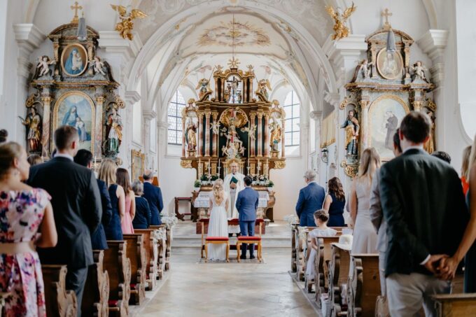 Eine Hochzeitszeremonie in einer Kirche, bei der Menschen den Mittelgang entlanggehen.