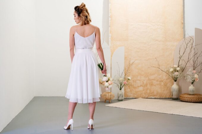 Eine Frau in einem weißen Kleid steht in einem leeren Raum.