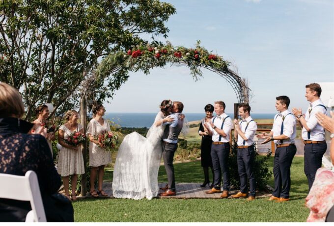 Eine Hochzeitszeremonie, bei der sich Braut und Bräutigam vor dem Meer küssen.