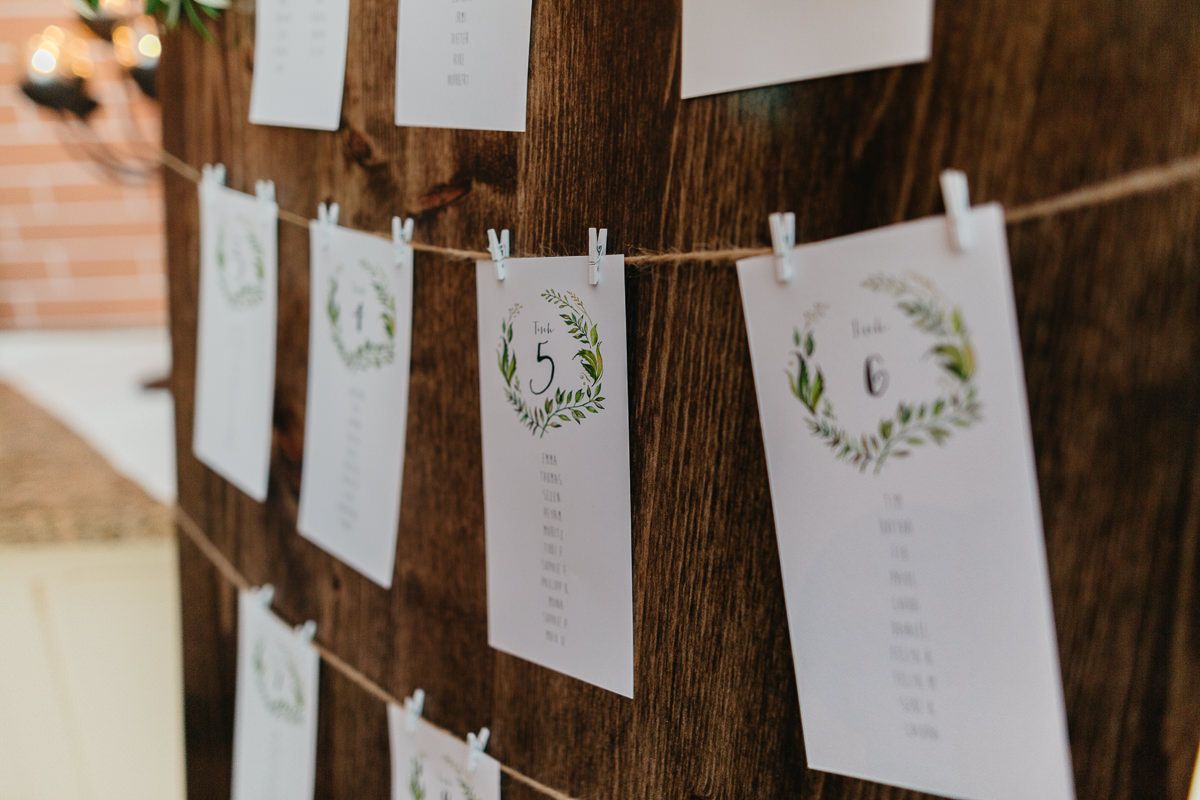 Hochzeitssitzplan mit Grünpflanzen, die an einem Holzbrett hängen.