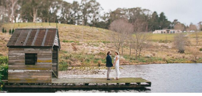 Eine Braut und ein Bräutigam stehen auf einem Steg an einem See.