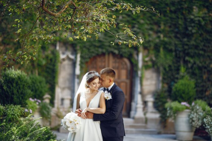 Eine Braut und ein Bräutigam umarmen sich vor einer mit Efeu bedeckten Wand.