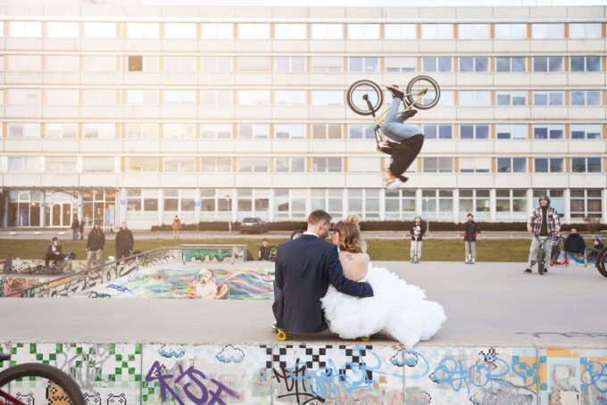 Eine Braut und ein Bräutigam machen Tricks auf einem Skateboard vor einem Gebäude.