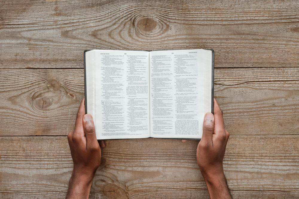 Hände halten eine aufgeschlagene Bibel auf einem Holztisch.