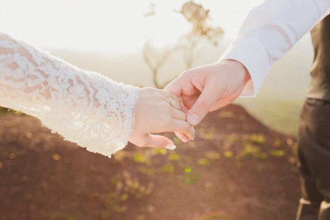 Eine Braut und ein Bräutigam halten sich an den Händen auf einem Hügel.