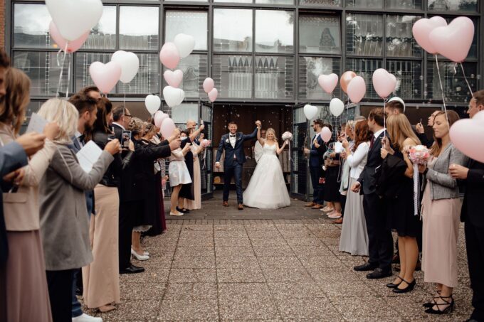 Eine Braut und ein Bräutigam gehen mit rosa Luftballons den Altar entlang.