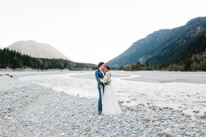 Eine Braut und ein Bräutigam stehen an einem Fluss in den Bergen.