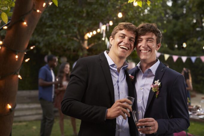 Zwei Männer in Anzügen lächeln sich auf einer Party an.