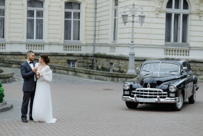 Ein Brautpaar posiert vor einem alten Auto.