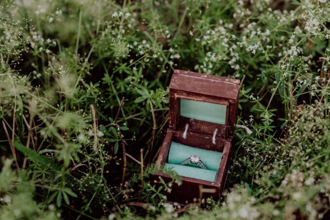 Ein Verlobungsring liegt in einer Holzkiste im Gras.