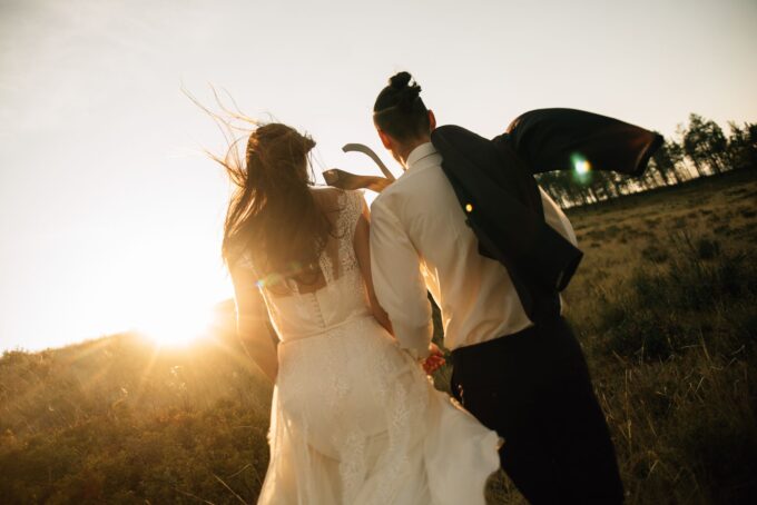 Eine Braut und ein Bräutigam gehen bei Sonnenuntergang durch ein Feld.
