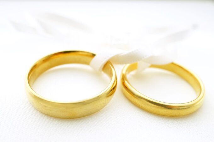 Zwei goldene Eheringe auf einer weißen Oberfläche.
