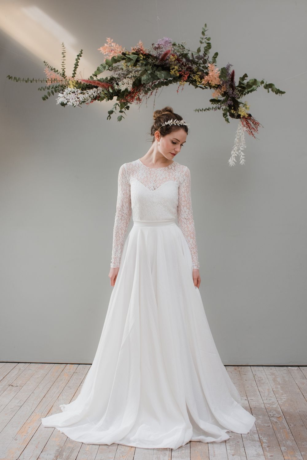 Eine Braut in einem langärmeligen Brautkleid steht vor einer Holzwand.