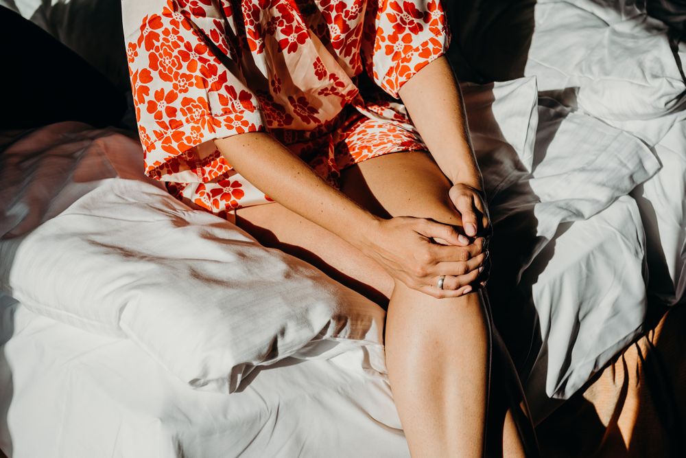 Eine Frau sitzt mit gekreuzten Beinen auf einem Bett.