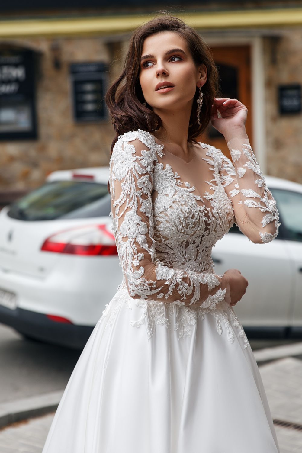 Eine Frau in einem weißen Hochzeitskleid steht vor einem Auto.