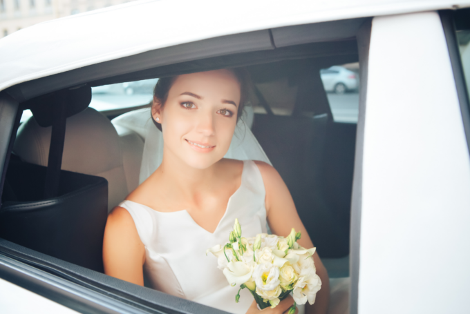 Eine Braut sitzt auf dem Rücksitz eines Autos.