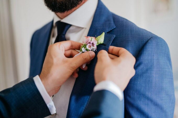Ein Mann im blauen Anzug steckt sich eine Ansteckblume an.