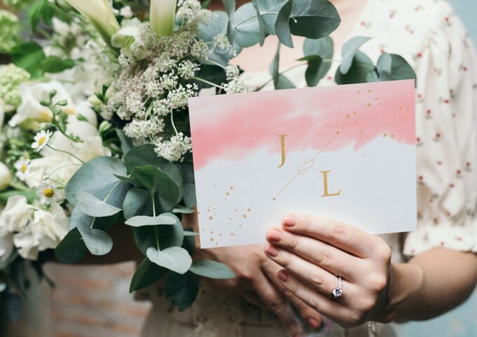 Eine Braut hält eine rosa-goldene Hochzeitskarte hoch.