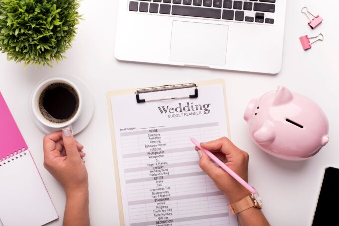 Eine Frau schreibt ein Hochzeitsbudget auf ein Klemmbrett mit einem rosa Sparschwein.