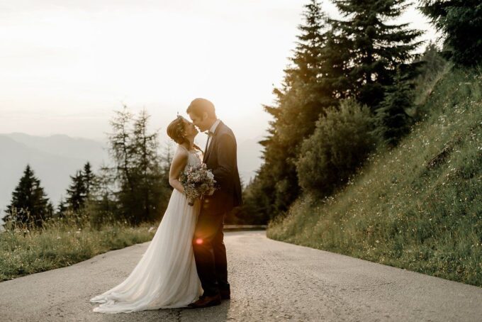 Eine Braut und ein Bräutigam küssen sich auf einer Straße in den Bergen.