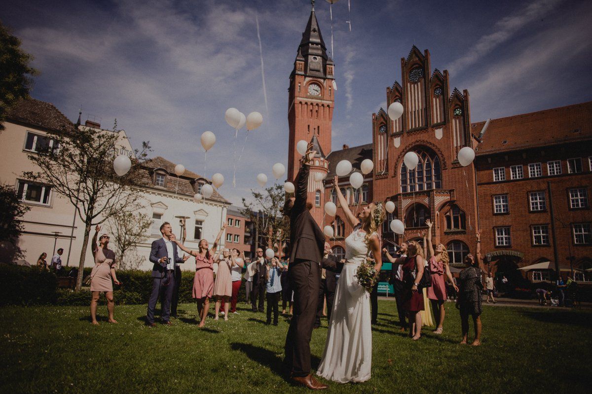 Ein Brautpaar wirft Luftballons vor einer Kirche.