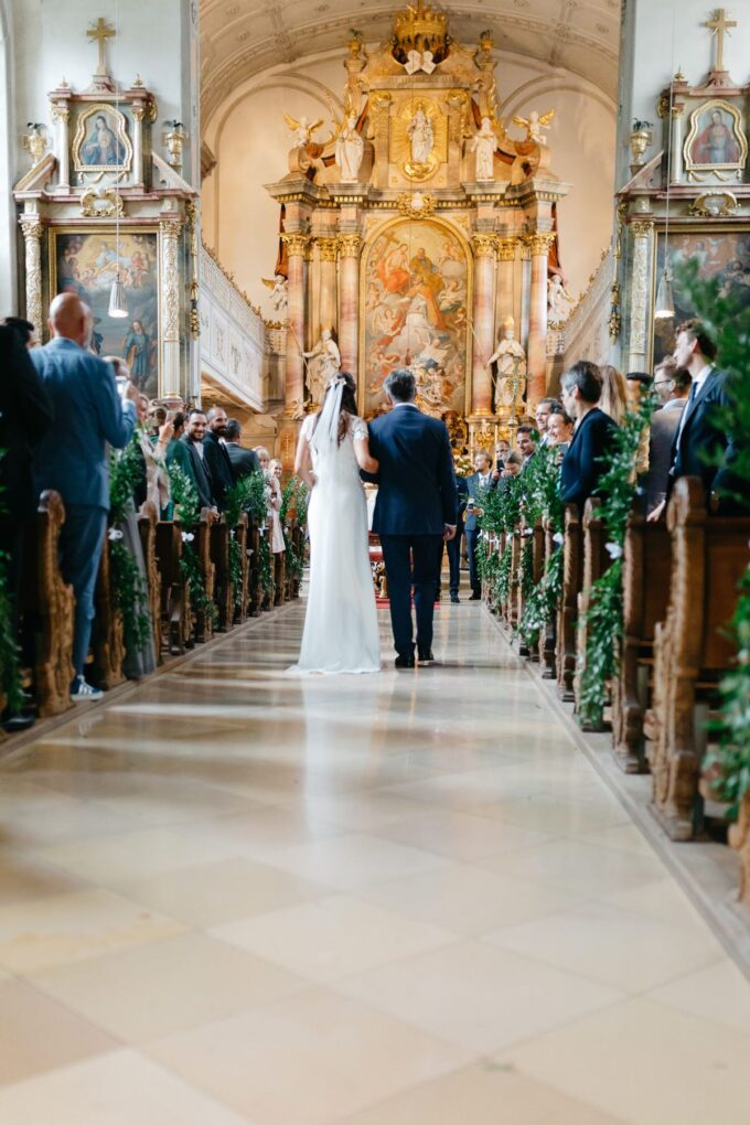 Eine Braut und ein Bräutigam gehen den Mittelgang einer Kirche entlang.