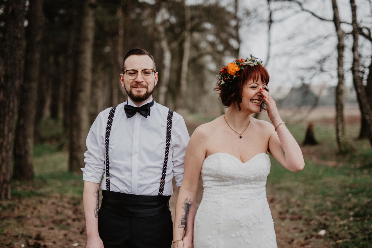 Brautpaar lacht im Wald und Braut hält sichd ie Hand vor Ihr Gesicht