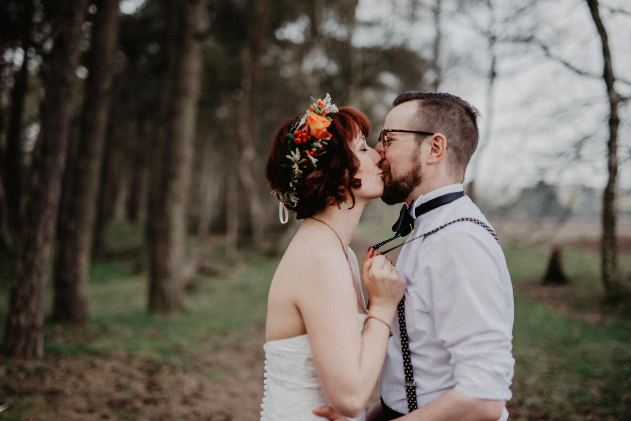 Brautpaar küssr sich und Braut hält sich an Hosenträgern des Bräutigams fest