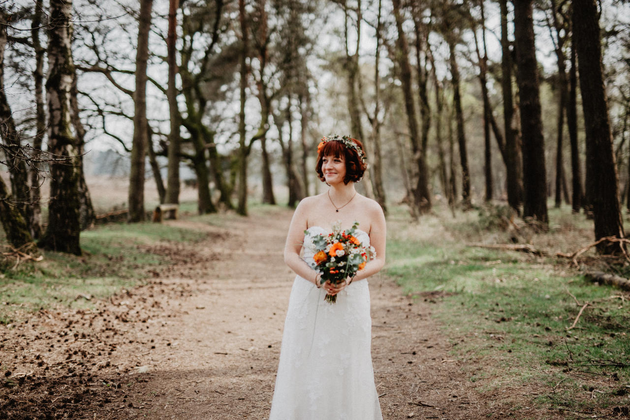 Braut steht im Wald mit Brautstrauß