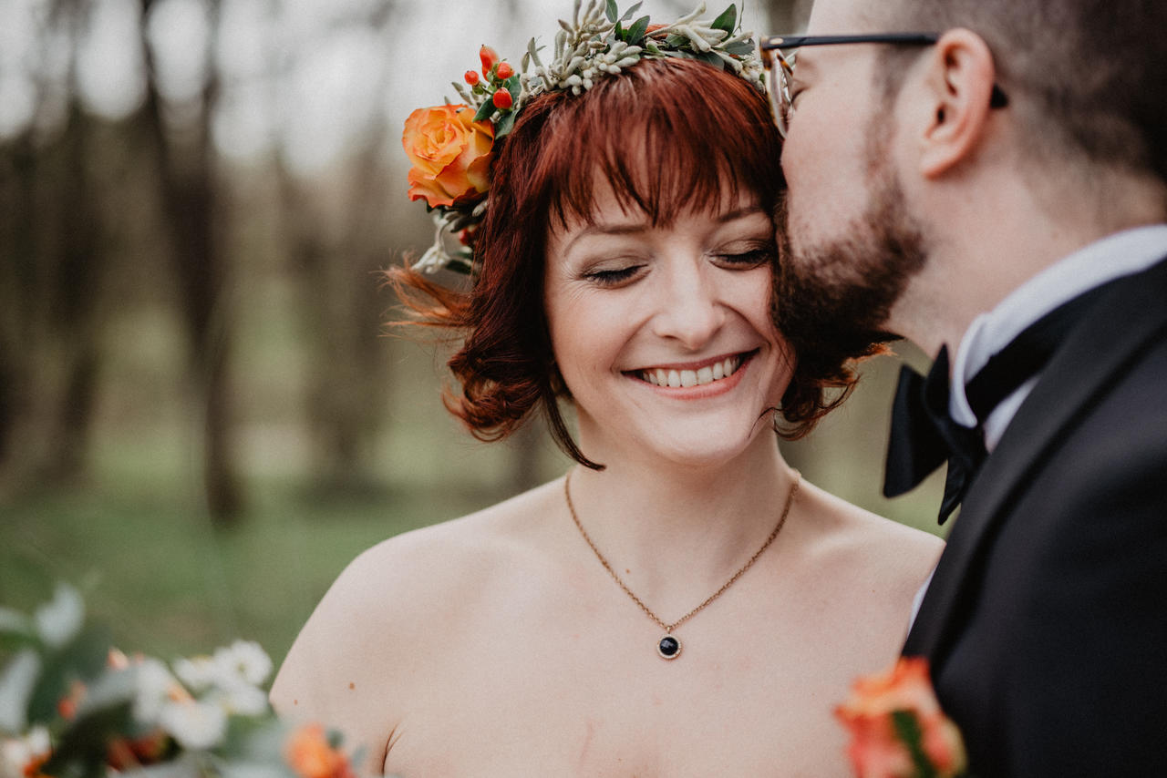 Bräutigam küsst Braut im Wald auf den Kopf