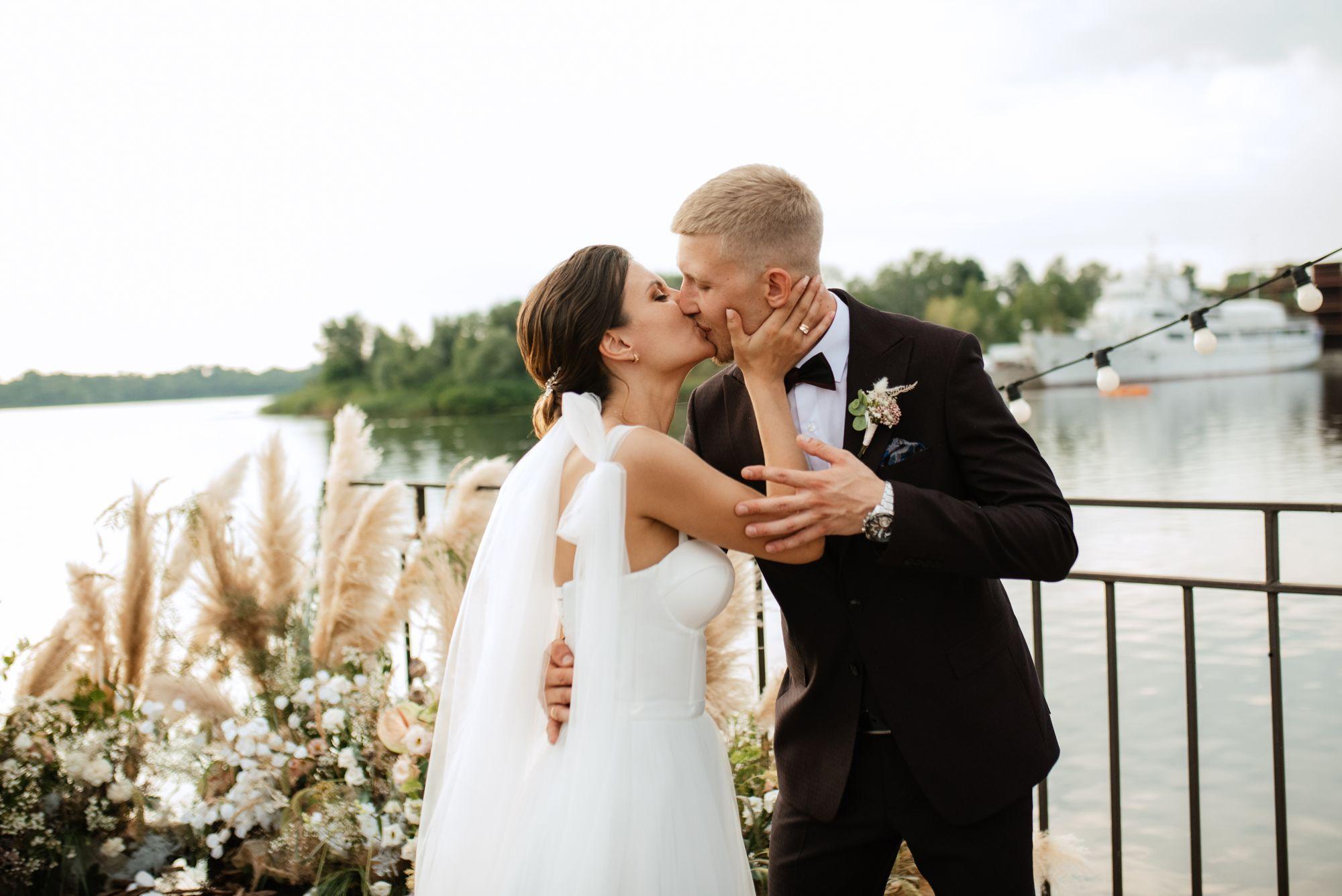 Eine Braut und ein Bräutigam küssen sich vor einem See.