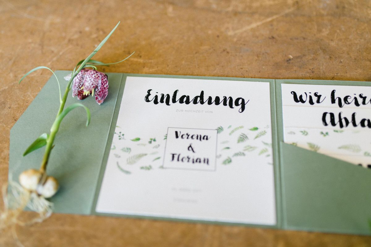 Eine grüne Hochzeitseinladung mit einer Blume darauf.