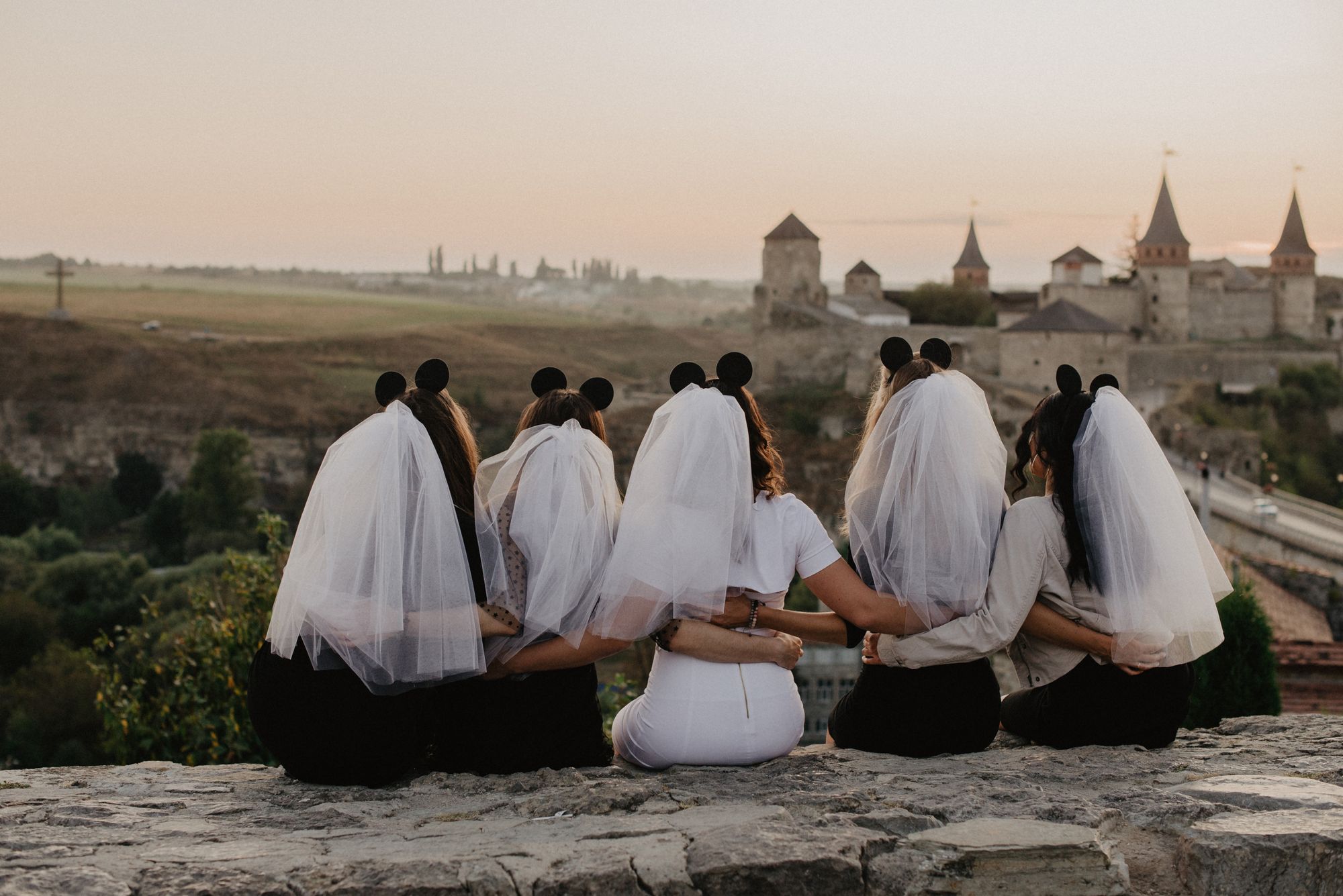 Eine Gruppe Brautjungfern sitzt auf einem Felsen mit Blick auf eine Burg.