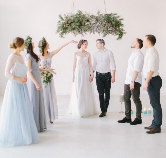 Eine Gruppe Brautjungfern und Bräutigam stehen vor einem Kranz.