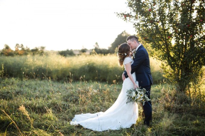 Eine Braut und ein Bräutigam umarmen sich bei Sonnenuntergang auf einem Feld.